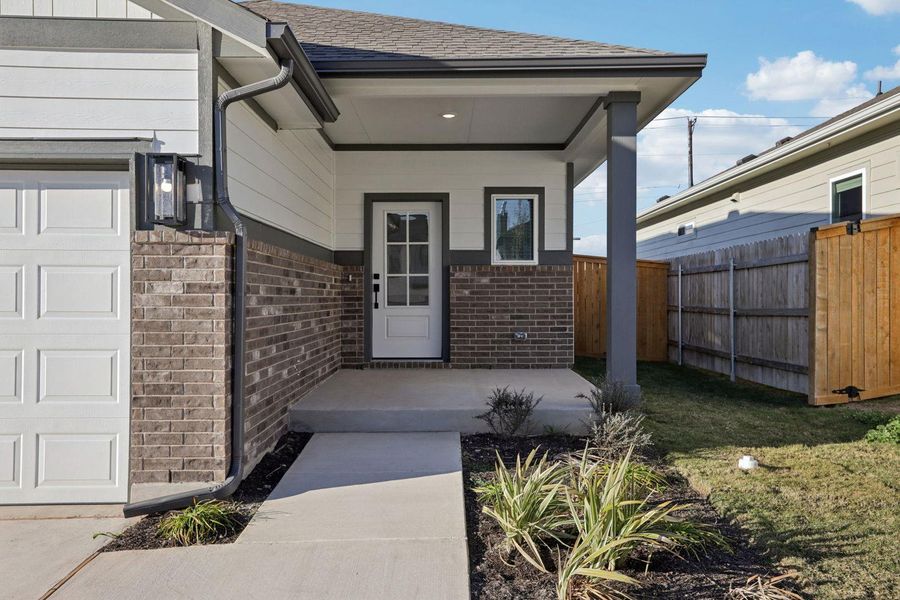 View of exterior entry featuring brick siding, a porch, and a shingled roof