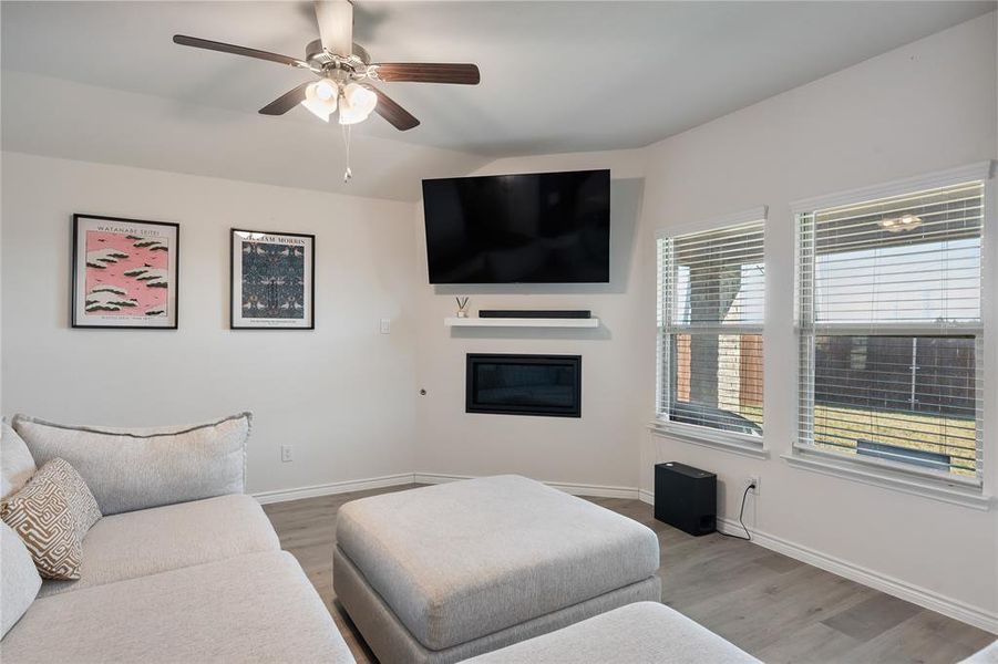 Living area featuring a glass covered fireplace, light wood finished floors, and a ceiling fan