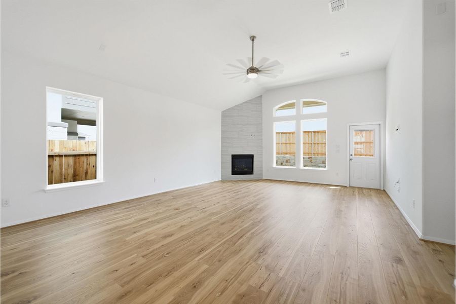 Unfurnished living room with a fireplace, lofted ceiling, a ceiling fan, and light wood-style floors