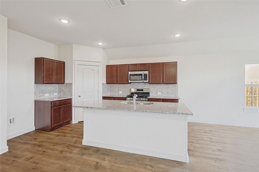 Kitchen featuring backsplash, stainless steel appliances, a kitchen island with sink, and hardwood / wood-style flooring