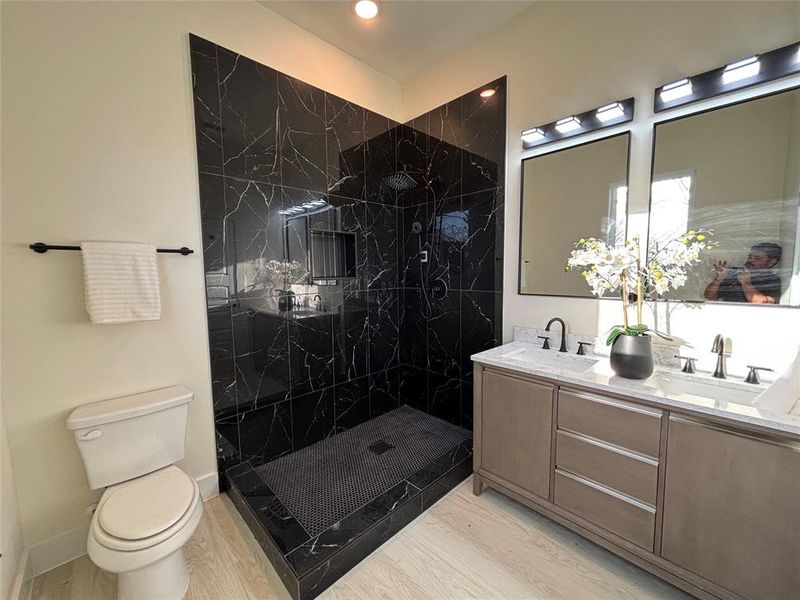 Bathroom featuring double vanity, a marble finish shower, and light wood-style flooring