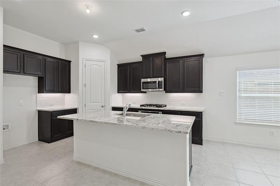 Kitchen with an island with sink, lofted ceiling, sink, tasteful backsplash, and appliances with stainless steel finishes