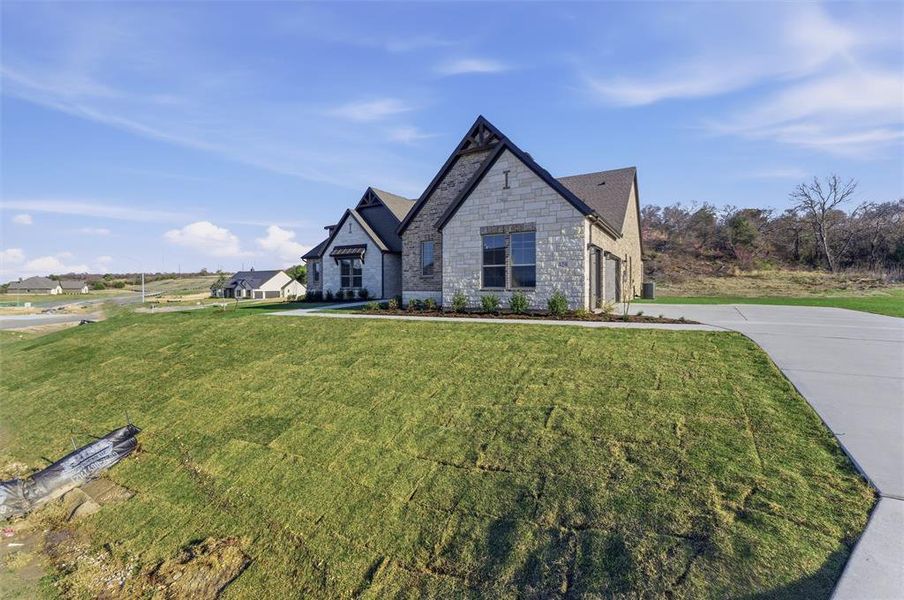 French country inspired facade featuring stone siding, a front yard, concrete driveway, and a garage