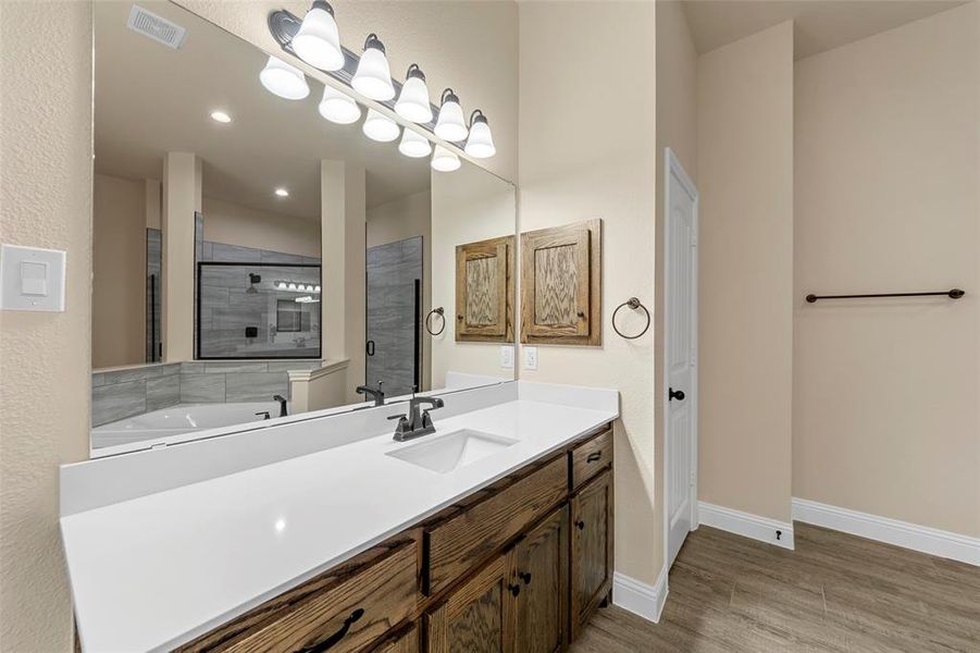 Bathroom with wood finished floors, baseboards, tiled shower, vanity, and recessed lighting