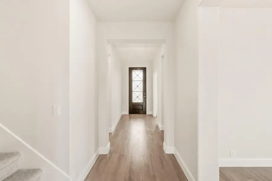 Narrow entryway hallway with hardwood floors, white walls, and dark front door with glass panels