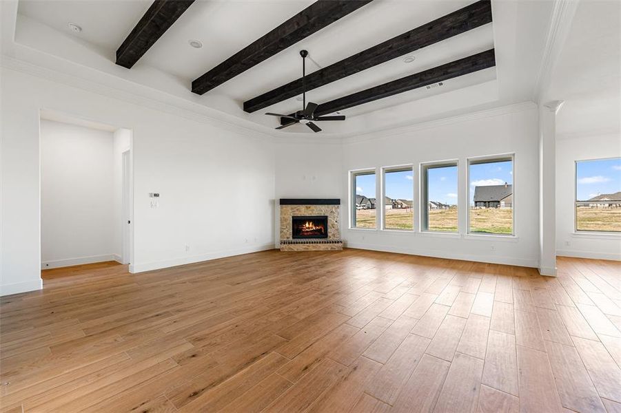 Unfurnished living room with a lit fireplace, light wood-style floors, a ceiling fan, and beam ceiling