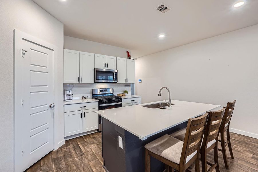 Kitchen with a sink, appliances with stainless steel finishes, a kitchen island with sink, and dark wood finished floors