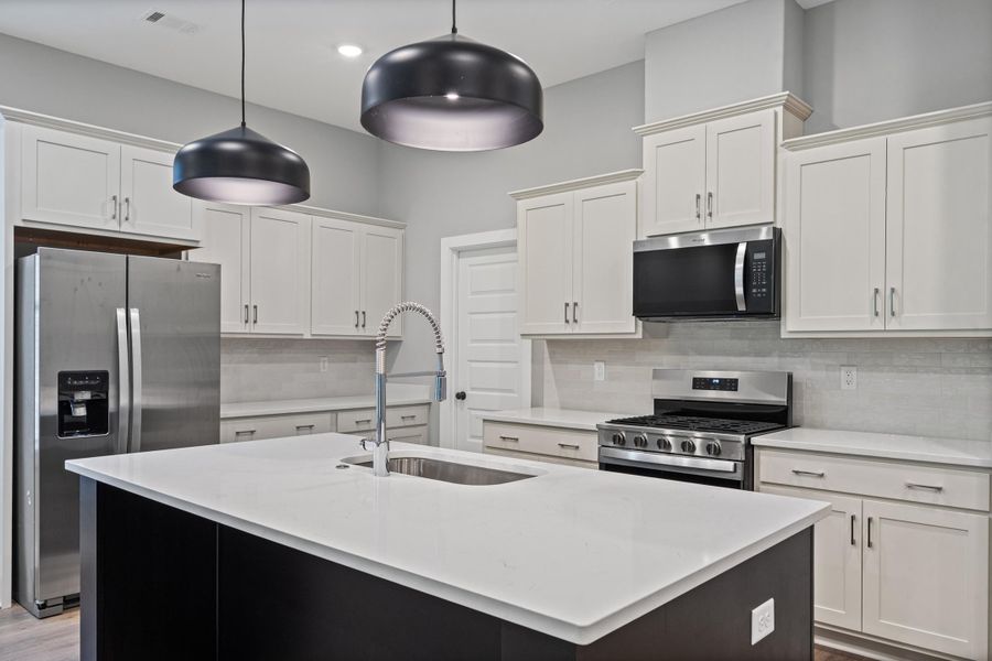 Kitchen featuring a large island with an integrated sink, pendant lighting, stainless steel appliances, white cabinetry, and a tile backsplash Kitchen featuring a large island with an integrated sink, pendant lighting, stainless steel appliances, white cabinetry, and a tile backsplash