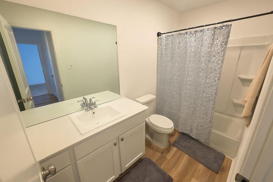 Full bathroom featuring dark wood finished floors, vanity, and shower / bathtub combination with curtain Full bathroom featuring dark wood finished floors, vanity, and shower / bathtub combination with curtain