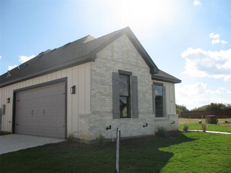 View of property exterior with board and batten siding, brick siding, a lawn, an attached garage, and concrete driveway