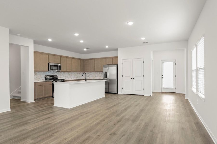 Kitchen featuring stainless steel appliances, light countertops, an island with sink, recessed lighting, and light wood-style floors