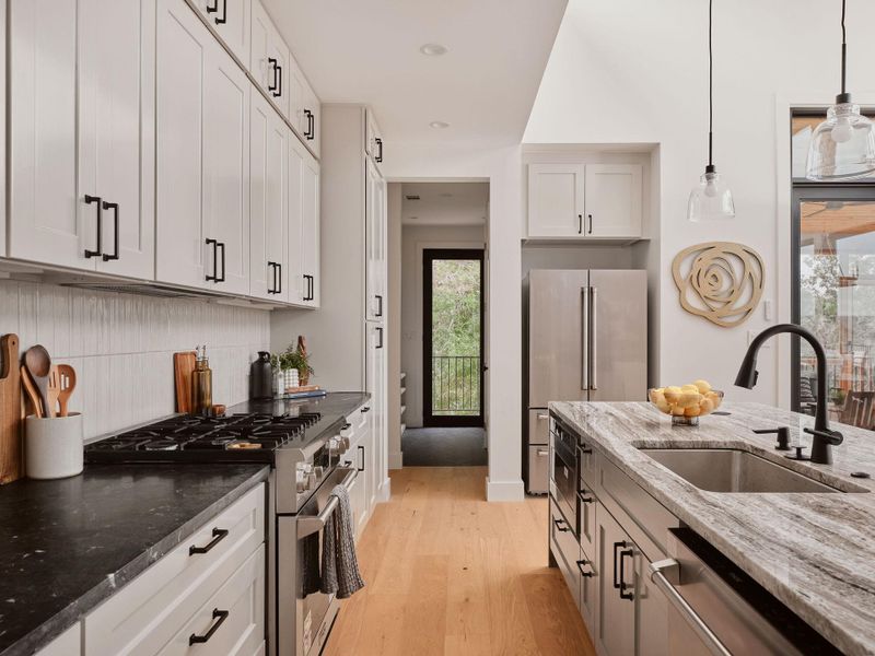 Contemporary kitchen featuring light wood-finish flooring, white shaker-style cabinetry with matte black hardware, and dark stone countertops