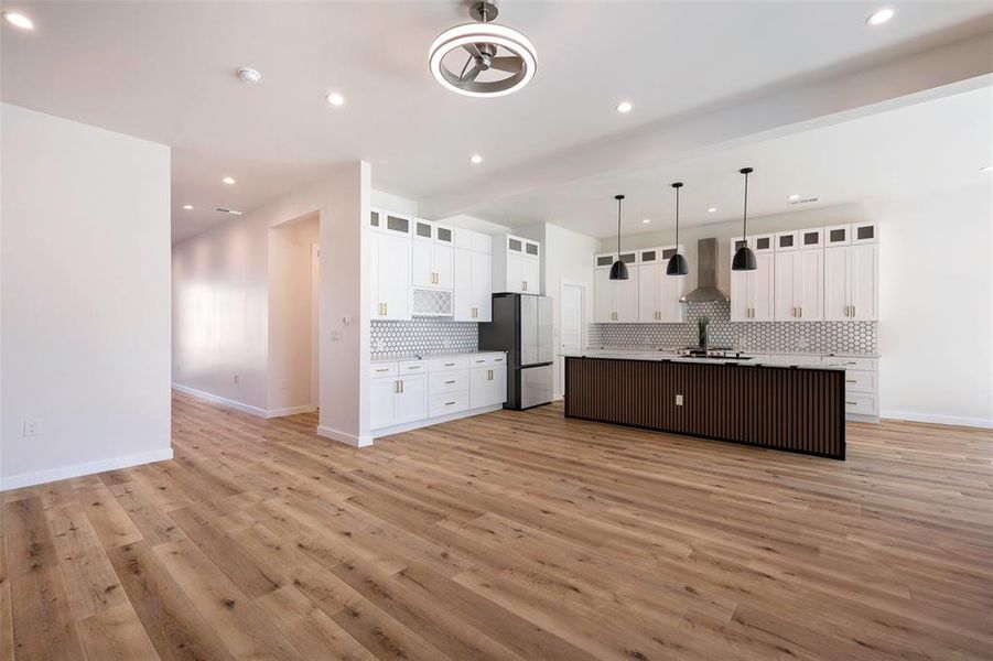 Kitchen with stainless steel refrigerator, light hardwood / wood-style flooring, backsplash, a center island with sink, and white cabinets