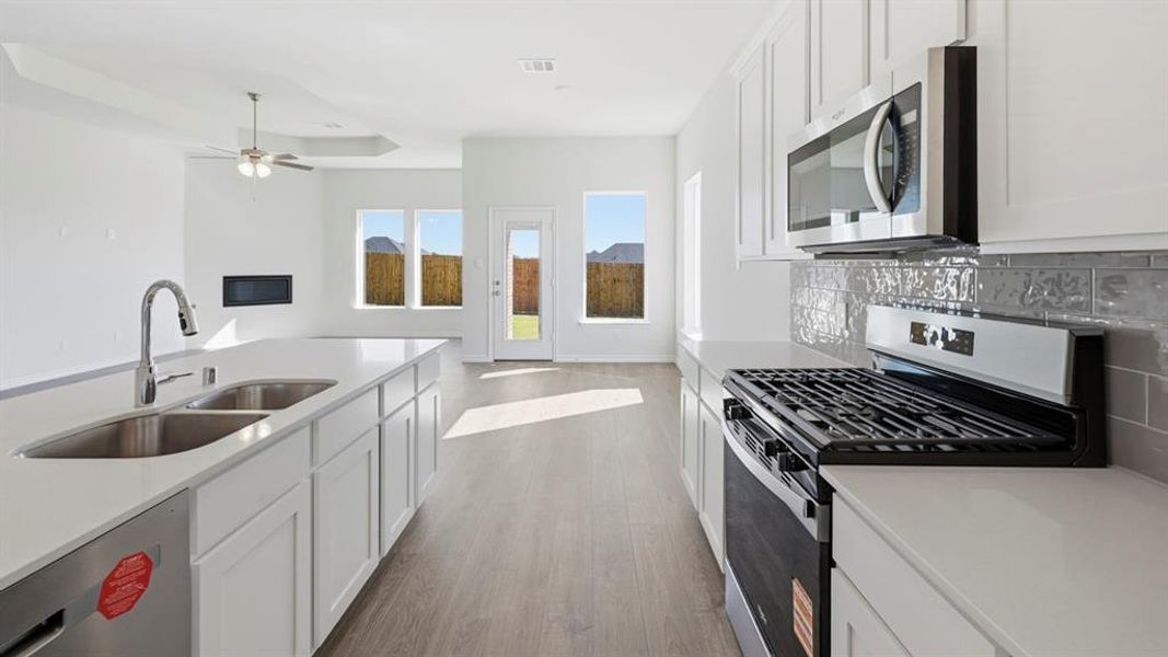Kitchen featuring a dual basin sink with a gooseneck faucet, light-toned countertops, and white cabinetry