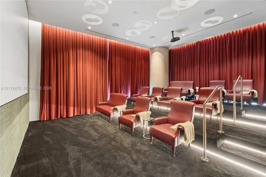 Tiered seating room featuring full-height drapery, recessed ceiling lighting, integrated audio speakers, and illuminated stair lighting