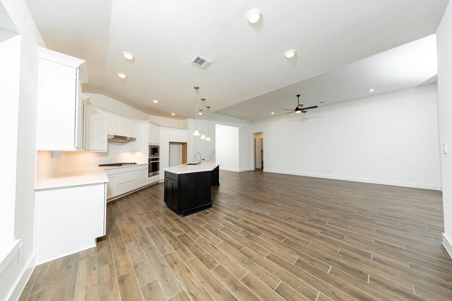 A spacious central island offers prep space and houses a sleek black undermount sink and a dishwasher. Recessed and contemporary pendant lights ensure a well-lit environment.