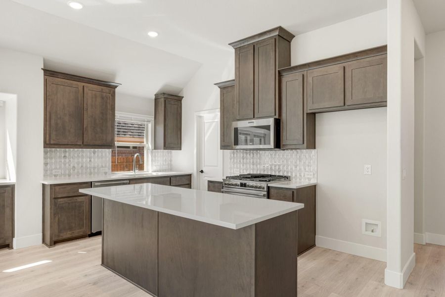 Kitchen with dark brown cabinets, center island, white countertops, and stainless steel appliances on light hardwood floors