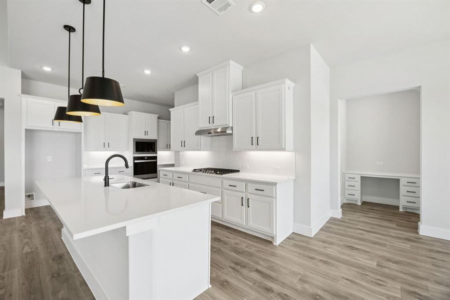 Kitchen with white cabinetry, a kitchen island with sink, pendant lighting, light wood finished floors, and recessed lighting