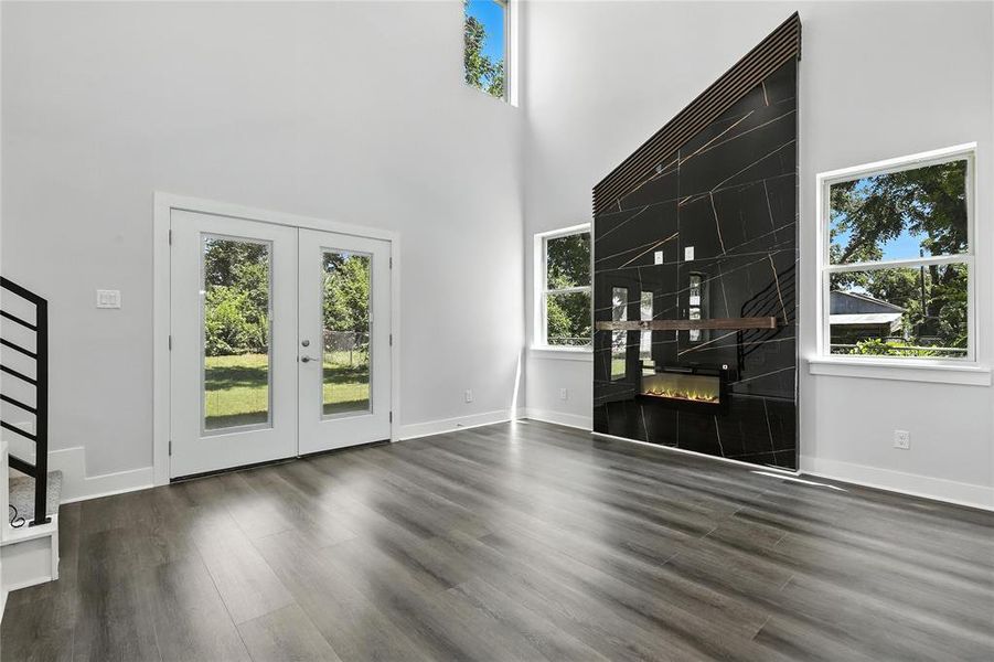 Unfurnished living room with a high ceiling, french doors, a tiled fireplace, and dark wood-type flooring