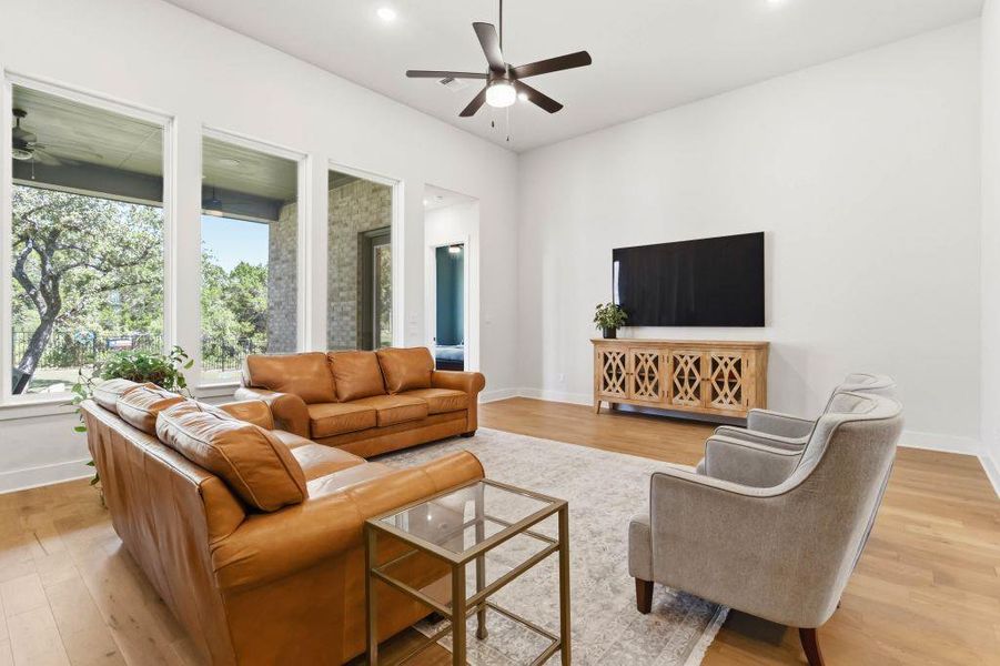 A spacious living room features light wood floors and large windows framing verdant trees, offering a tranquil indoor-outdoor connection.