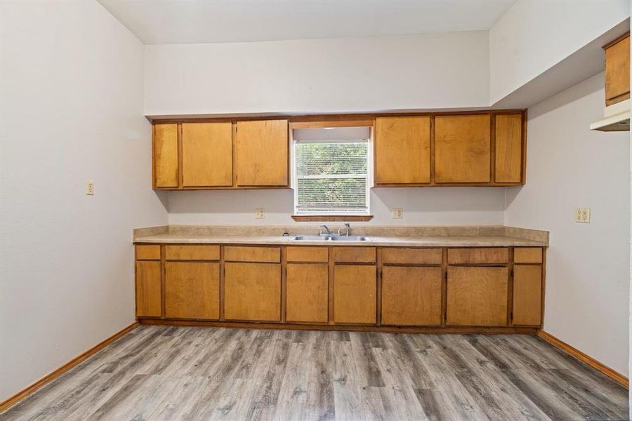 Kitchen featuring light countertops, brown cabinetry, light wood-style flooring, and under cabinet range hood Kitchen featuring light countertops, brown cabinetry, light wood-style flooring, and under cabinet range hood