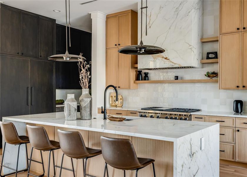 Kitchen featuring light stone countertops, decorative backsplash, light hardwood / wood-style floors, and decorative light fixtures