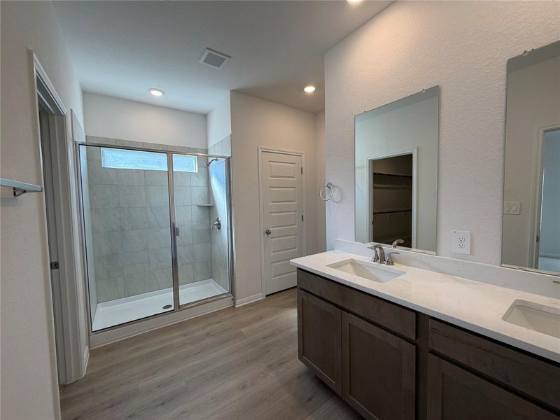 Full bath featuring a walk in closet, double vanity, a shower stall, and light wood-type flooring