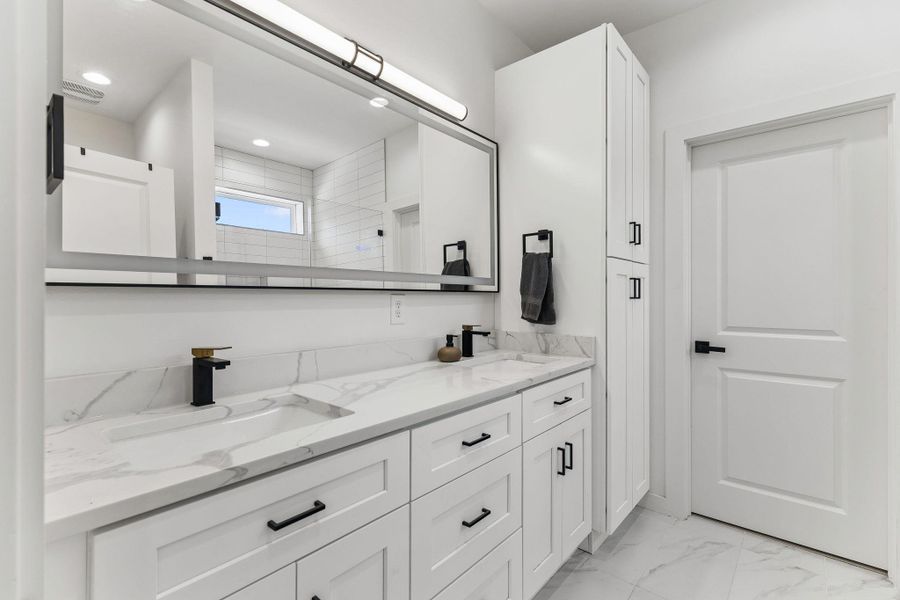 The primary ensuite bathroom exudes a spa-like vibe. It features a dual vanity with quartz countertops, modern rectangular under-mount sinks, and chic black-framed mirrors that pop against the light walls.