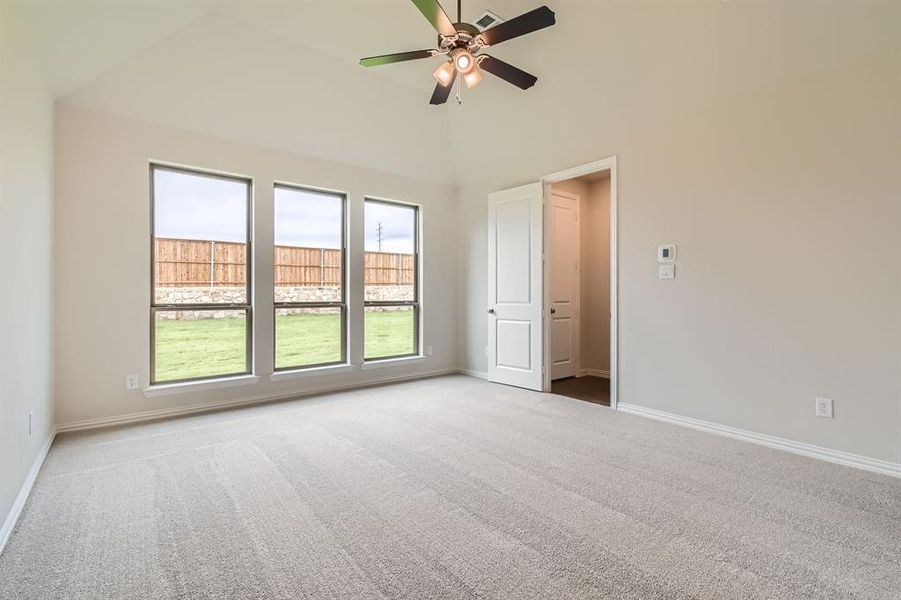 Carpeted empty room featuring ceiling fan and a high ceiling