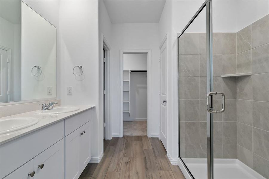 Bathroom with hardwood / wood-style floors, vanity with extensive cabinet space, an enclosed shower, and double sink
