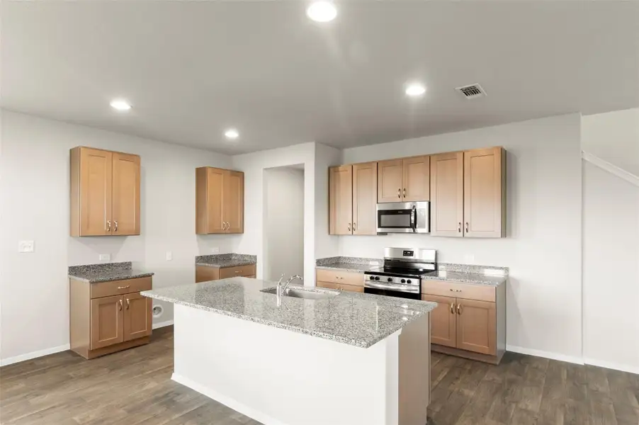 Kitchen featuring appliances with stainless steel finishes, dark wood finished floors, recessed lighting, a kitchen island with sink, and light stone countertops