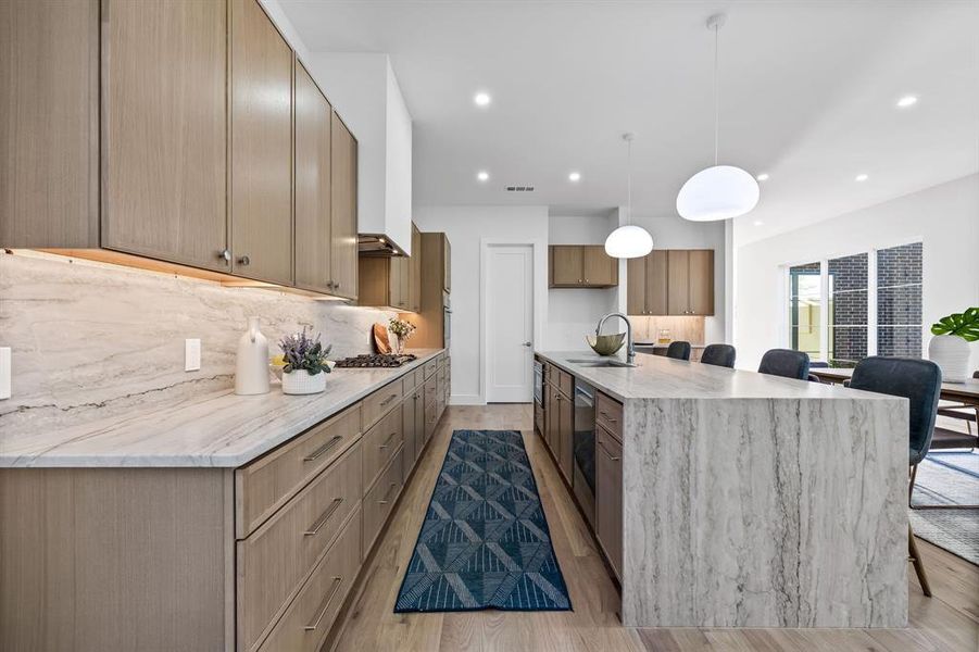 Kitchen with light wood-type flooring, backsplash, light stone counters, sink, and pendant lighting