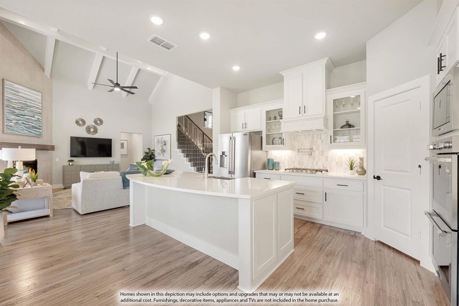 Open-concept kitchen with white cabinets, large island, and hardwood floors, open to living room with vaulted ceiling and fireplace.