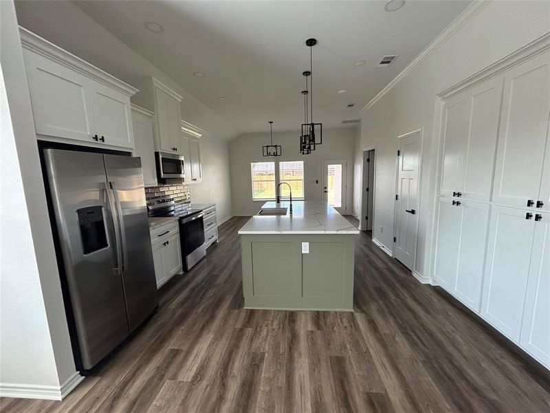 Kitchen featuring appliances with stainless steel finishes, a center island with sink, white cabinetry, dark wood-style flooring, and crown molding