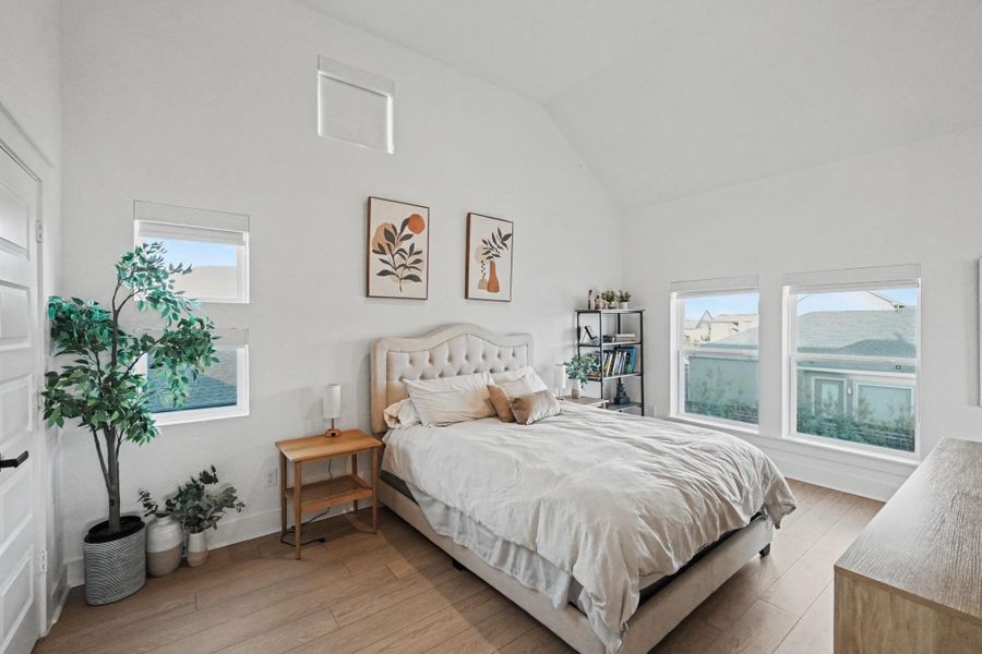 Spacious bedroom with vaulted ceilings and multiple windows that fill the room with natural light. The airy layout and warm flooring create a bright, comfortable retreat.