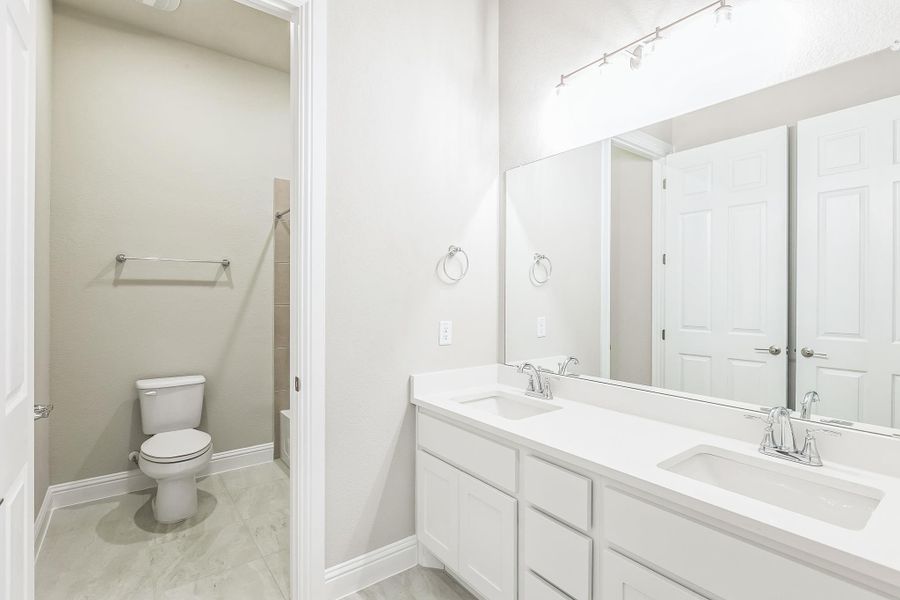 Full bath with double vanity, baseboards, a sink, and toilet Full bath with double vanity, baseboards, a sink, and toilet