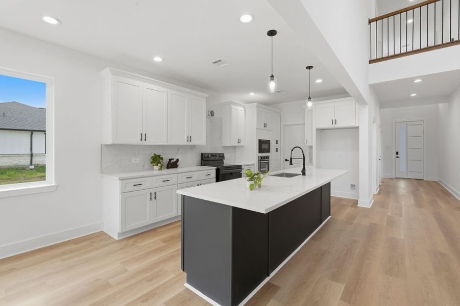 A modern kitchen featuring a large island with a sleek black base and Quartz countertops. The space includes soft closed cabinetry, stainless steel appliances, and pendant lighting. The light wood flooring and open layout create a bright and inviting atmosphere.