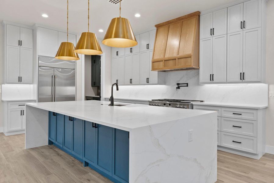 An inviting kitchen showcasing a bold blue island with pristine countertops and warm gold pendant lighting.