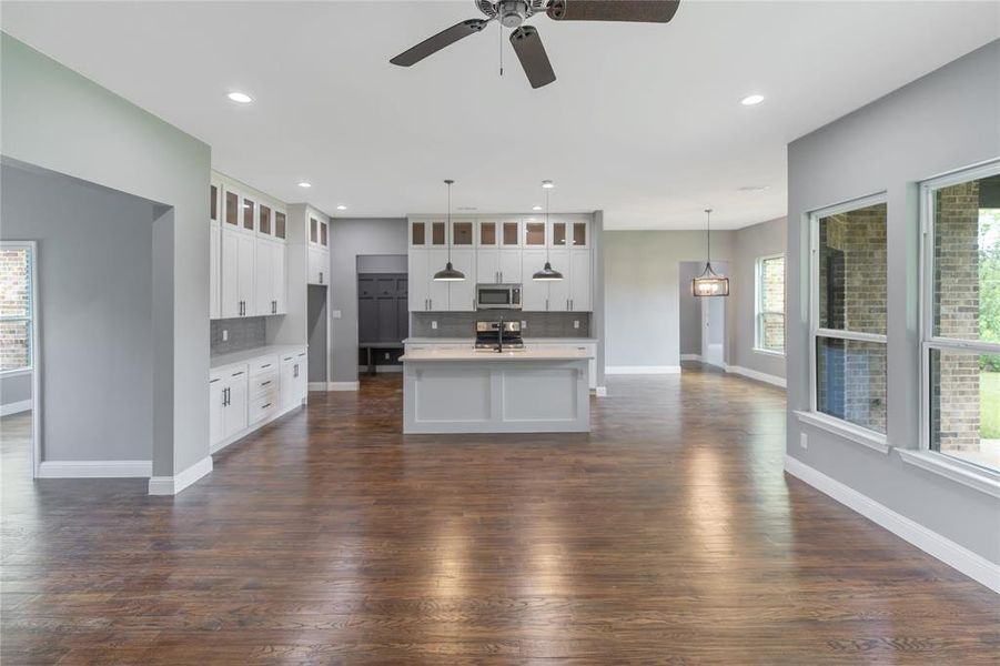 Kitchen featuring tasteful backsplash, glass insert cabinets, a center island with sink, dark wood finished floors, and ceiling fan Kitchen featuring tasteful backsplash, glass insert cabinets, a center island with sink, dark wood finished floors, and ceiling fan