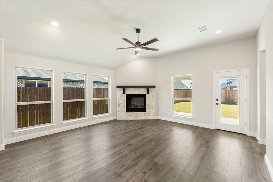 Open living room with stone fireplace, hardwood floors, ceiling fan, and backyard access door