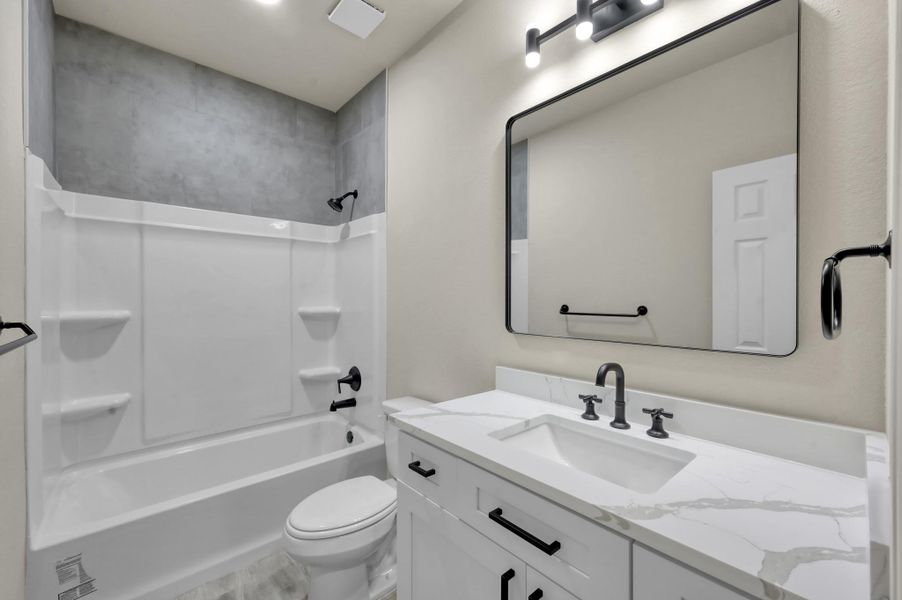 The second bathroom continues the home’s sophisticated theme with a sleek white vanity, marbled quartz counters, and a full tub/shower combo accented by modern gray tile and matte black hardware.