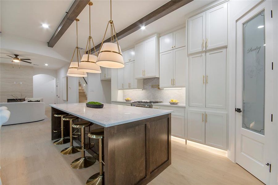 Kitchen featuring white cabinetry, arched walkways, light wood-style floors, decorative light fixtures, and a center island