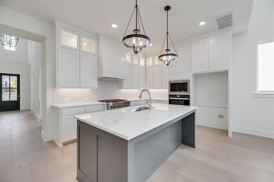 Kitchen with white cabinets, tasteful backsplash, a center island with sink, light wood finished floors, and glass insert cabinets