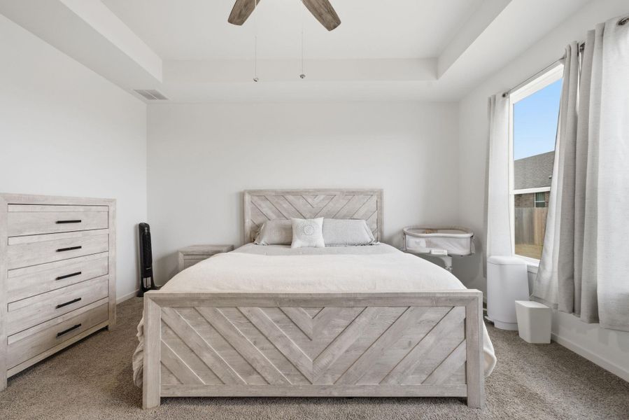 Carpeted bedroom with a tray ceiling and a ceiling fan