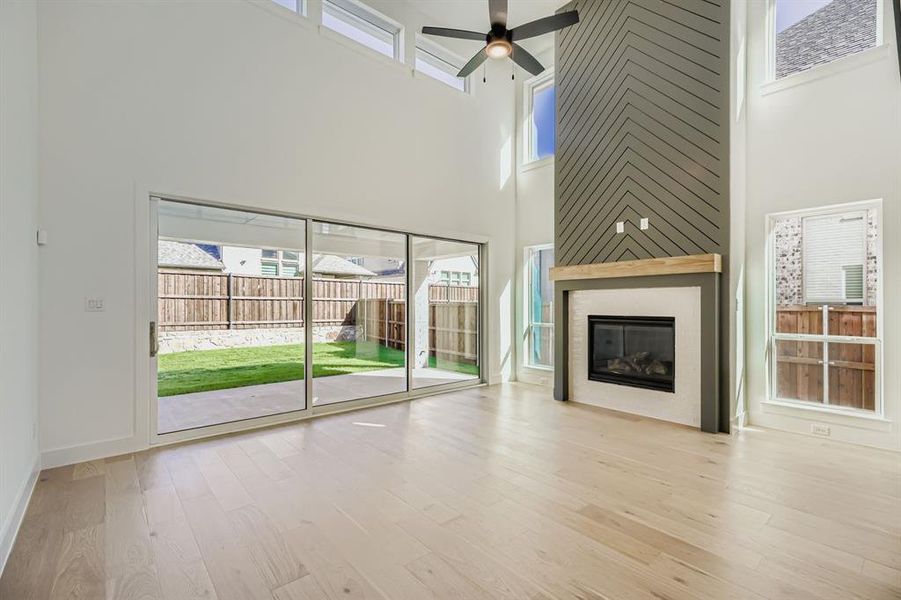 Unfurnished living room featuring light wood-style flooring, a high ceiling, a large fireplace, and a ceiling fan Unfurnished living room featuring light wood-style flooring, a high ceiling, a large fireplace, and a ceiling fan