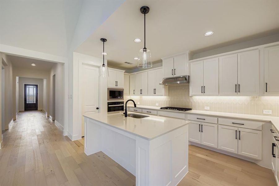 Kitchen with white cabinetry, light wood-type flooring, an island with sink, and stainless steel appliances
