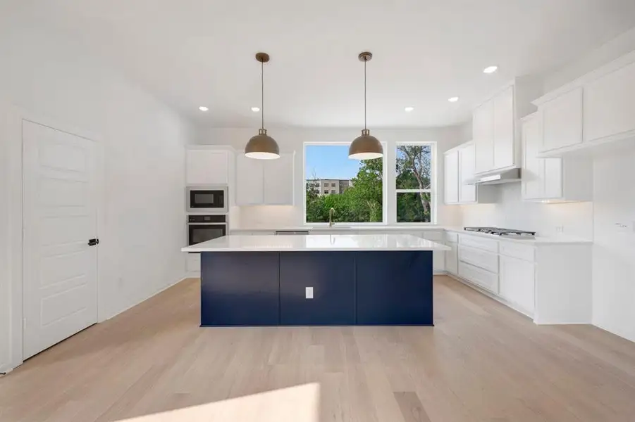 Contemporary kitchen featuring a prominent blue island with a white countertop, recessed lighting, wood-finish flooring, and white cabinetry