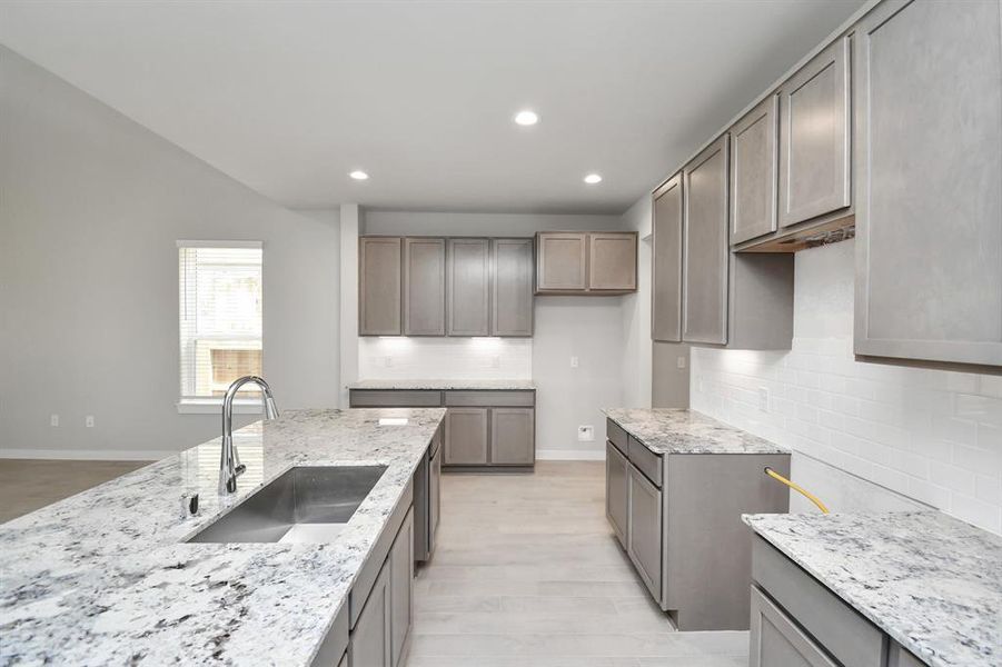 Discover another perspective of this stunning kitchen, sleek back splash, single basin sink, and generously appointed with an abundance of counter space. Sample photo, as built color and selections will vary.