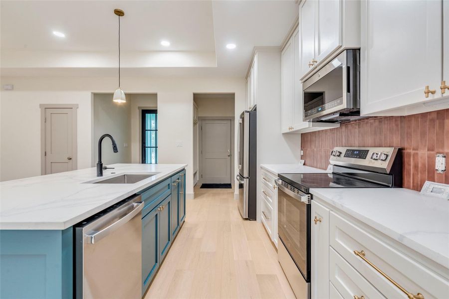 Kitchen with blue cabinetry, appliances with stainless steel finishes, white cabinets, light stone countertops, and recessed lighting