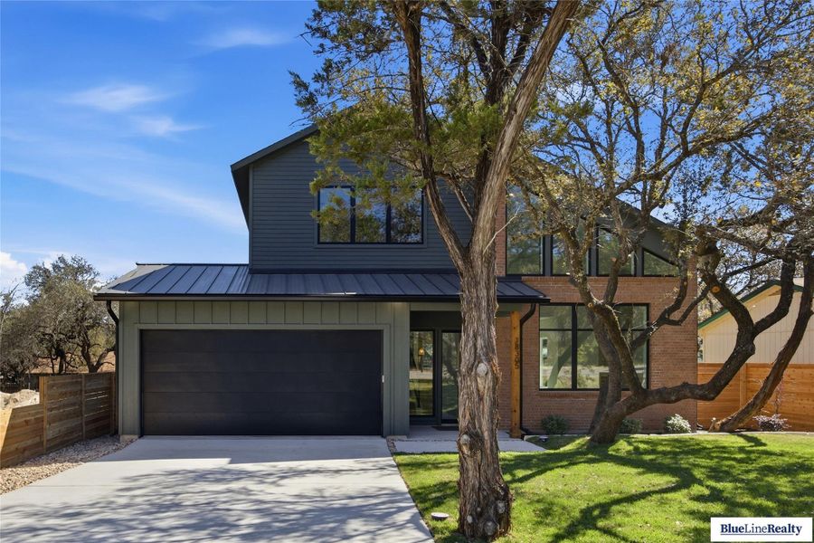 View of front of property featuring driveway, board and batten siding, a standing seam roof, and brick siding